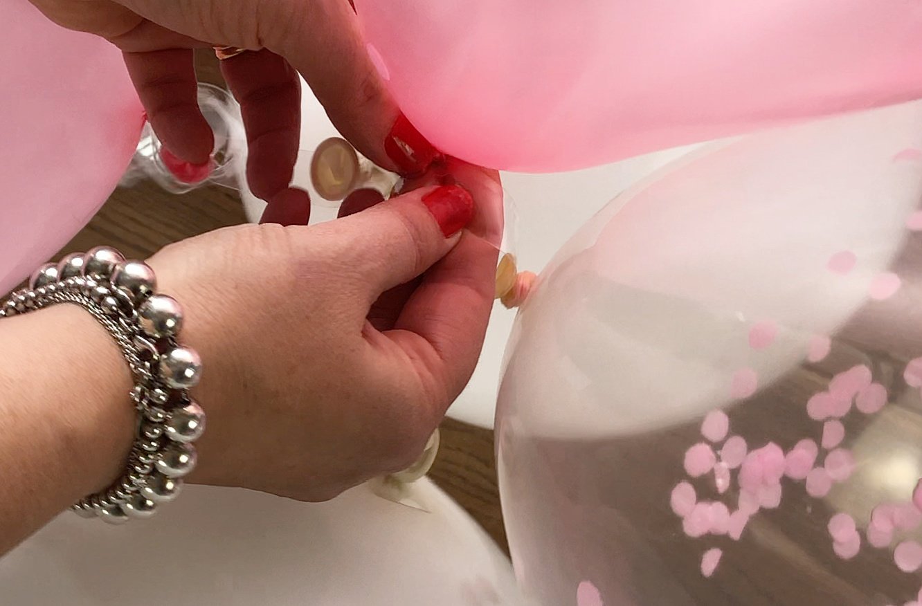 pull the balloon knots through the hole on the balloon strip tape to secure them ensuring you space out your larger balloons